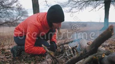 女孩游客在徒步旅行时在秋天的森林里篝火。 为烹饪和温暖而燃烧。 徒步旅行的概念